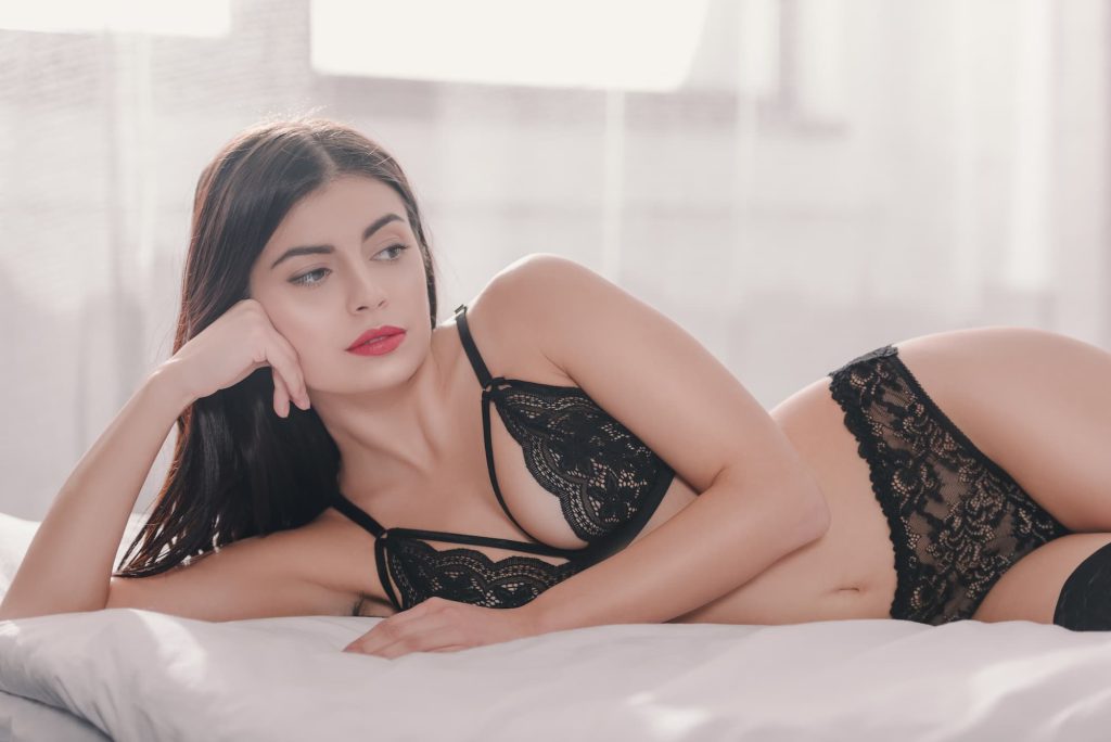 Giovane ragazza sexy in lingerie nera in camera da letto sdraiata sul letto.